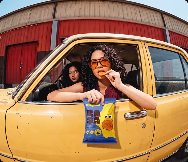 Perempuan di mobil kuning memegang RASA Chips